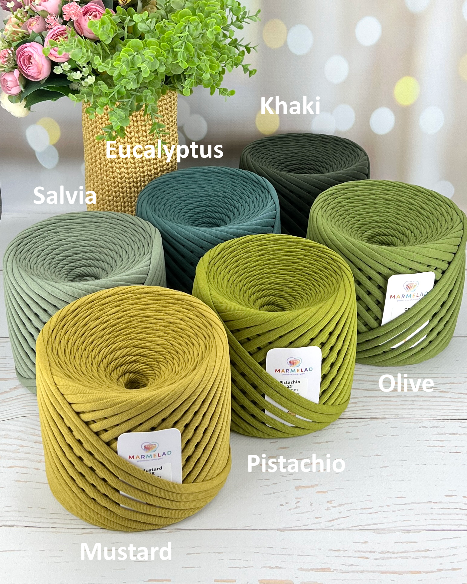 Assorted rolls of green yarn with color labels on a wooden surface.