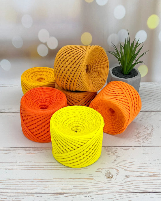 Five rolls of yellow, orange, and red rope on a wooden surface with a blurred background.
