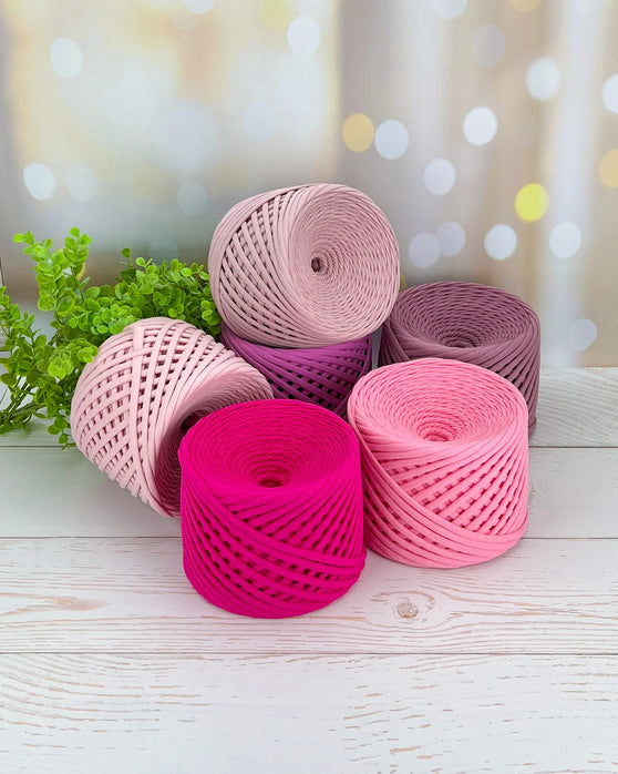 Five rolls of pink and purple yarn on a wooden surface with a blurred background