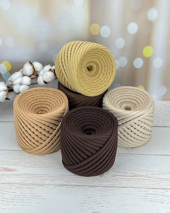 Four spools of beige, brown, and white yarn on a wooden surface with a blurred background.