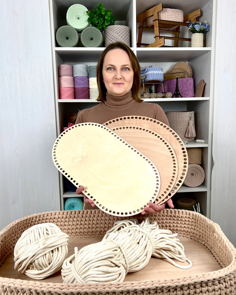 Woman holding two circular wooden frames in a craft room with shelves of yarn and materials.