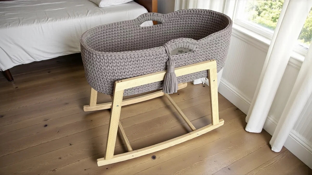 Gray woven baby crib on a wooden stand in a bedroom setting.